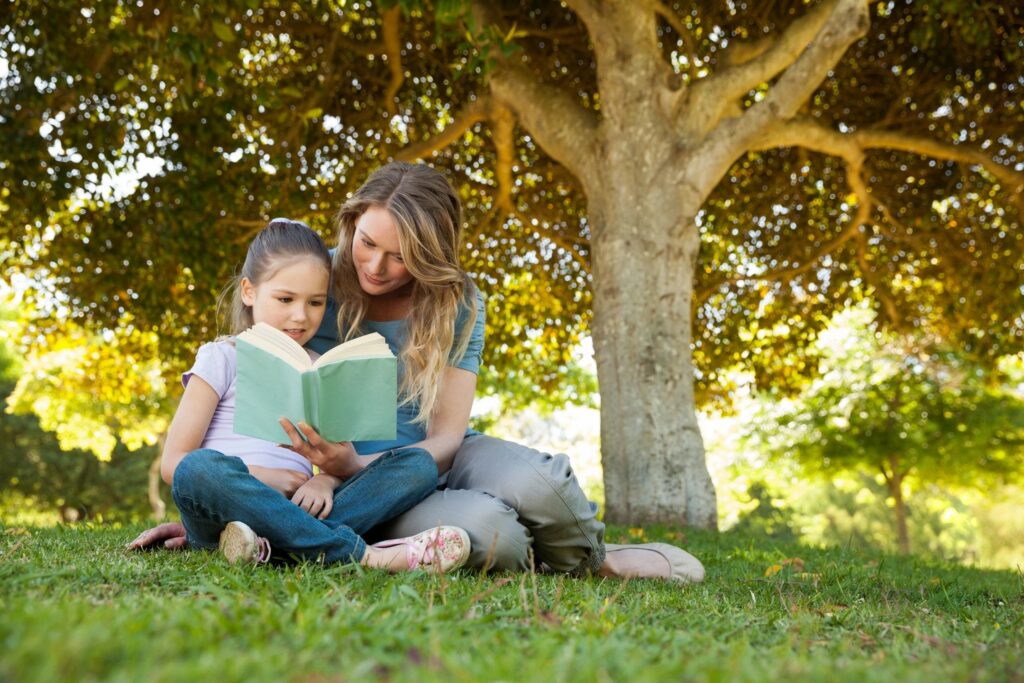 Adult and child reading under a tree